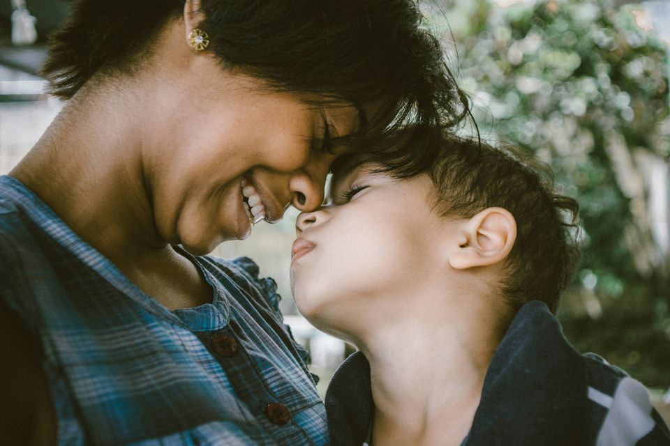 A mother and her young son touch noses and smile at each other.
