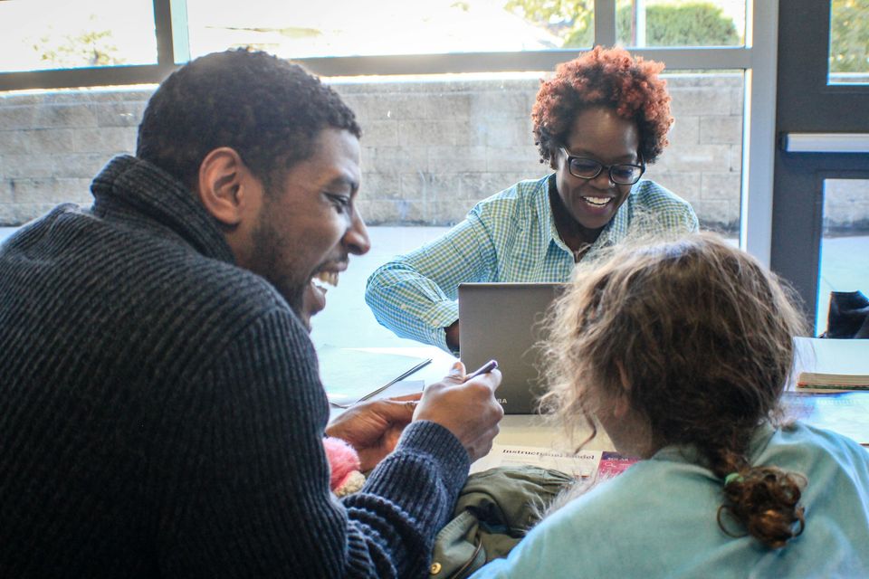 A man and a woman sit at a table with a young girl, looking over papers and a laptop together.